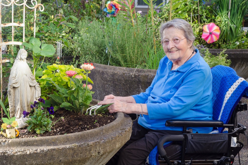 A happy elderly woman in an assisted-living facility tends to her flowers in a wheelchair-accessible garden container.